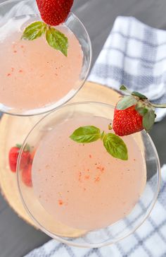 two martinis with strawberries on the rim and garnished with basil leaves