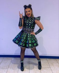 a woman in a green and blue dress posing for the camera with her finger up