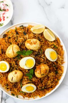 a white plate topped with fried eggs and rice next to a bowl of lemon wedges