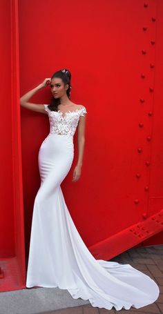 a woman in a white dress leaning against a red wall