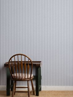 a wooden chair sitting in front of a wall with vertical stripes on it's walls