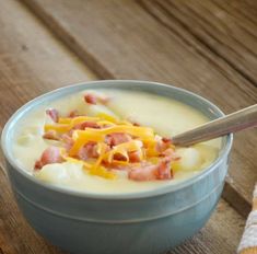 a bowl of soup with cheese and bacon in it next to a napkin on a wooden table