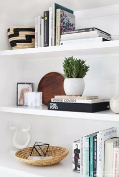 some books and plants are on the shelves in this white bookcase with wicker baskets