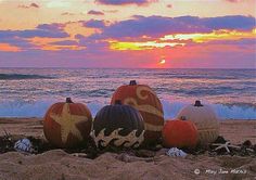 three pumpkins are sitting on the sand near the ocean as the sun goes down