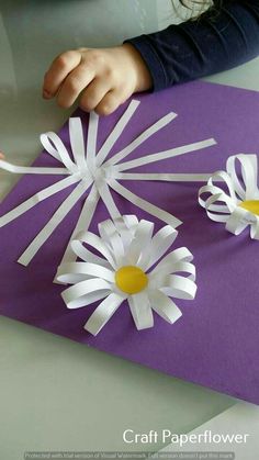 a child cutting out paper flowers on top of a piece of purple and white paper