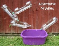 several empty plastic water bottles floating in the air over a purple container on grass next to a wooden fence