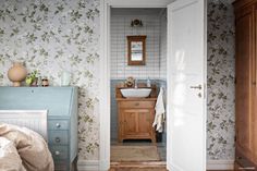 a bathroom with floral wallpaper and wooden cabinet in the corner, along with a white sink