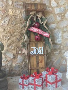 christmas decorations on display in front of a stone wall with red bows and presents underneath