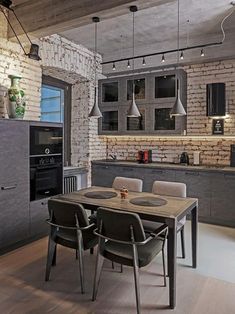 a dining room table and chairs in front of a brick wall with lights hanging from the ceiling