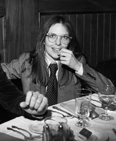 two people sitting at a table with wine glasses in front of them and one person holding something up to her mouth