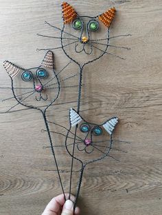 a person is holding some wire art with cats on it's head and another cat made out of beads