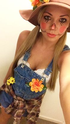 a woman in overalls and a hat with flowers on her head is taking a selfie