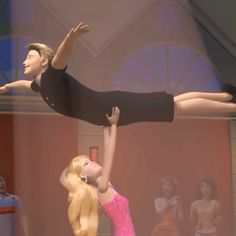 two barbie dolls standing on their heads and arms in the air, one holding onto another doll's leg