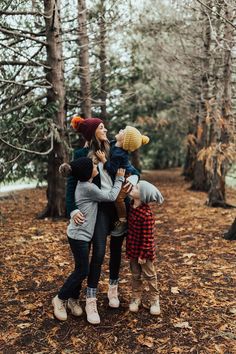 three people are standing in the woods with one holding two small children and smiling at the camera