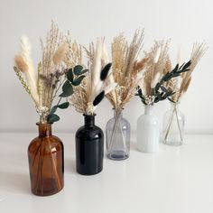 three vases with dried plants in them on a table