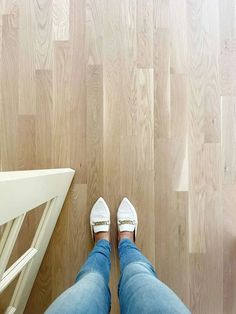 a person wearing white shoes and jeans standing on a wooden floor next to a chair