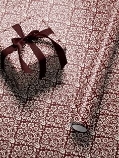 a wrapped present box sitting on top of a red and white table cloth with a brown ribbon