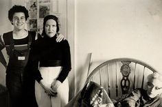 two women standing next to each other near a bed with an old fashioned headboard