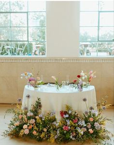 a table with flowers and greenery on it in front of large windows at a wedding reception