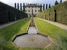 a large house with hedges surrounding it and a small pond in the middle of the yard