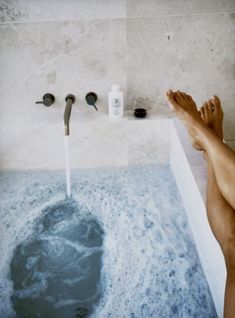 a person's feet in a bathtub with water running from the faucet