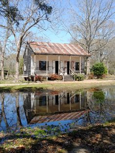 an old house sitting next to a pond in the middle of a field with trees