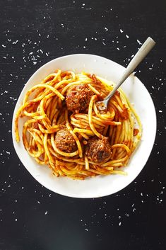 a white bowl filled with spaghetti and meatballs on top of a black countertop