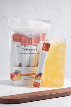 an orange juice and some white sticks in a bag on a wooden tray next to a drink