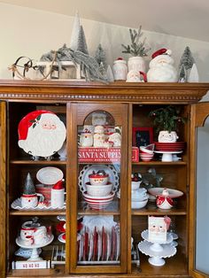 a wooden china cabinet filled with christmas dishes and santa clause hats on top of it