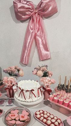 a table topped with lots of heart shaped cakes and cupcakes next to a pink bow