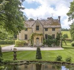 a large house sitting on top of a lush green field next to a pond in front of it