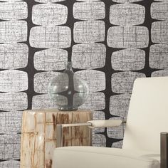 a white chair sitting in front of a wall with black and white designs on it