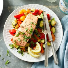 a white plate topped with salmon and veggies next to a glass of water