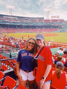 two women in red sox shirts and white shorts posing for the camera at a baseball game