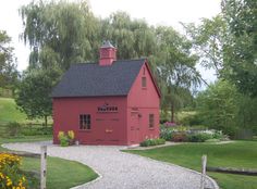 a red barn sits in the middle of a grassy area with flowers and trees around it