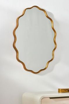 a round mirror hanging on the wall above a white dresser and cabinet with gold trim