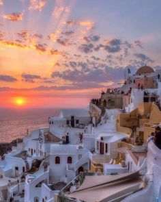 the sun is setting over some white buildings by the ocean in oia, greece