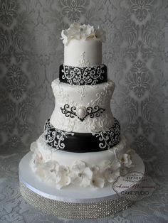 a three tiered wedding cake with white flowers and black ribbon on the bottom layer