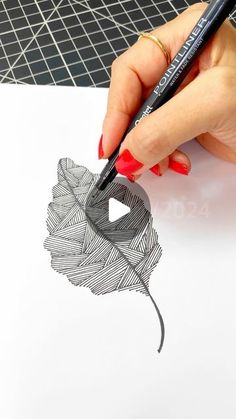 a woman's hand is holding a pencil and drawing a flower with black ink