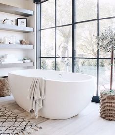 a large white bath tub sitting in a bathroom next to a window with open shelves