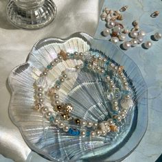 a glass plate with pearls and other jewelry on it next to a vase filled with beads