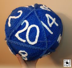 a person holding up a blue and white crochet d20 ball with the number twenty four on it