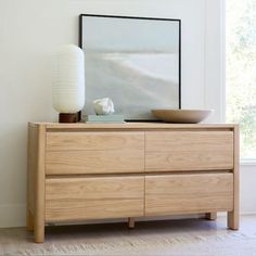 a wooden dresser sitting next to a window with a vase and bowl on top of it