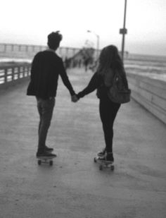 two people holding hands while skateboarding on the boardwalk