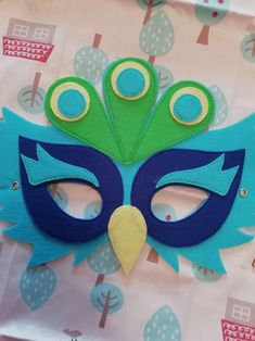 a blue mask with green feathers on top of a pink and white tableclothed background