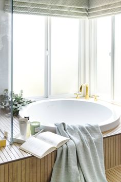 a white bath tub sitting under a window next to a book and cup on a table