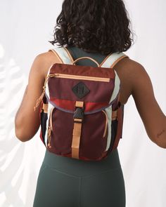 a woman with her back to the camera wearing a maroon and tan backpack that has straps on it