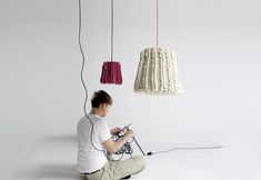 a person sitting on the ground with a remote in front of two knitted lamps