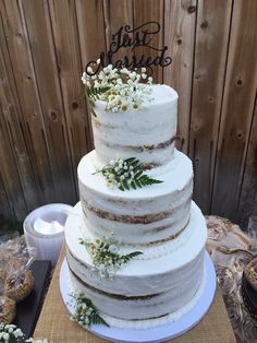 a three tiered cake with flowers and leaves on the top is displayed in front of a wooden fence