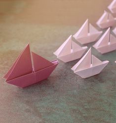 several paper boats are lined up on the floor and one is pink with white sails